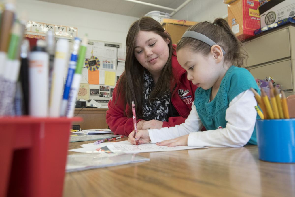 Female Reading Corps tutor looks on as young girl writes