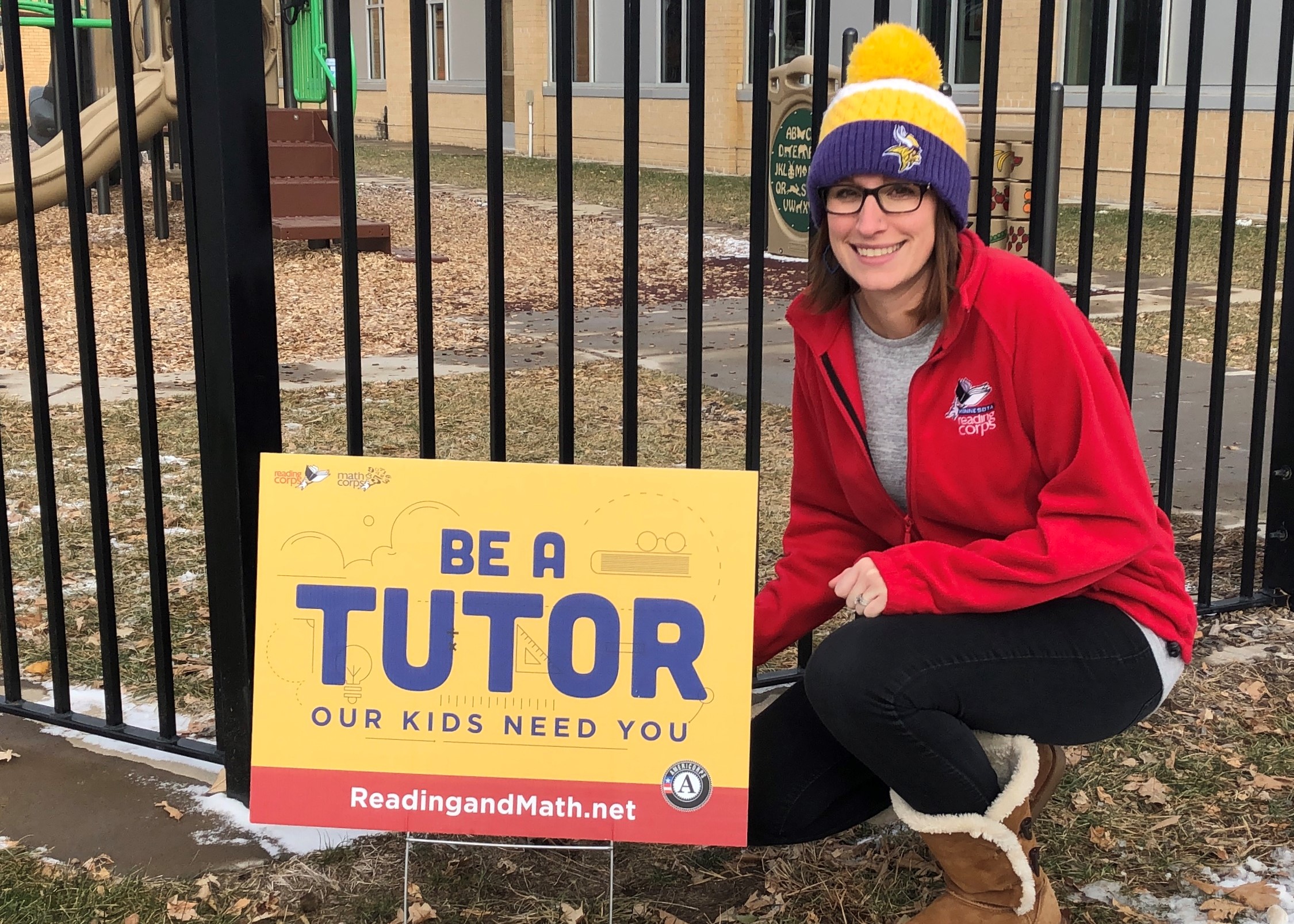 Reading Corps tutor Brianna poses next to yard sign which reads Be a Tutor