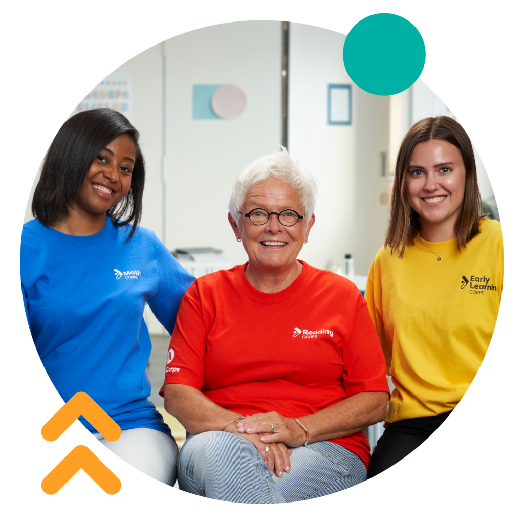 Three tutors in their Reading Corps, Math Corps, and Early Learning Corps gear smiling at the camera.