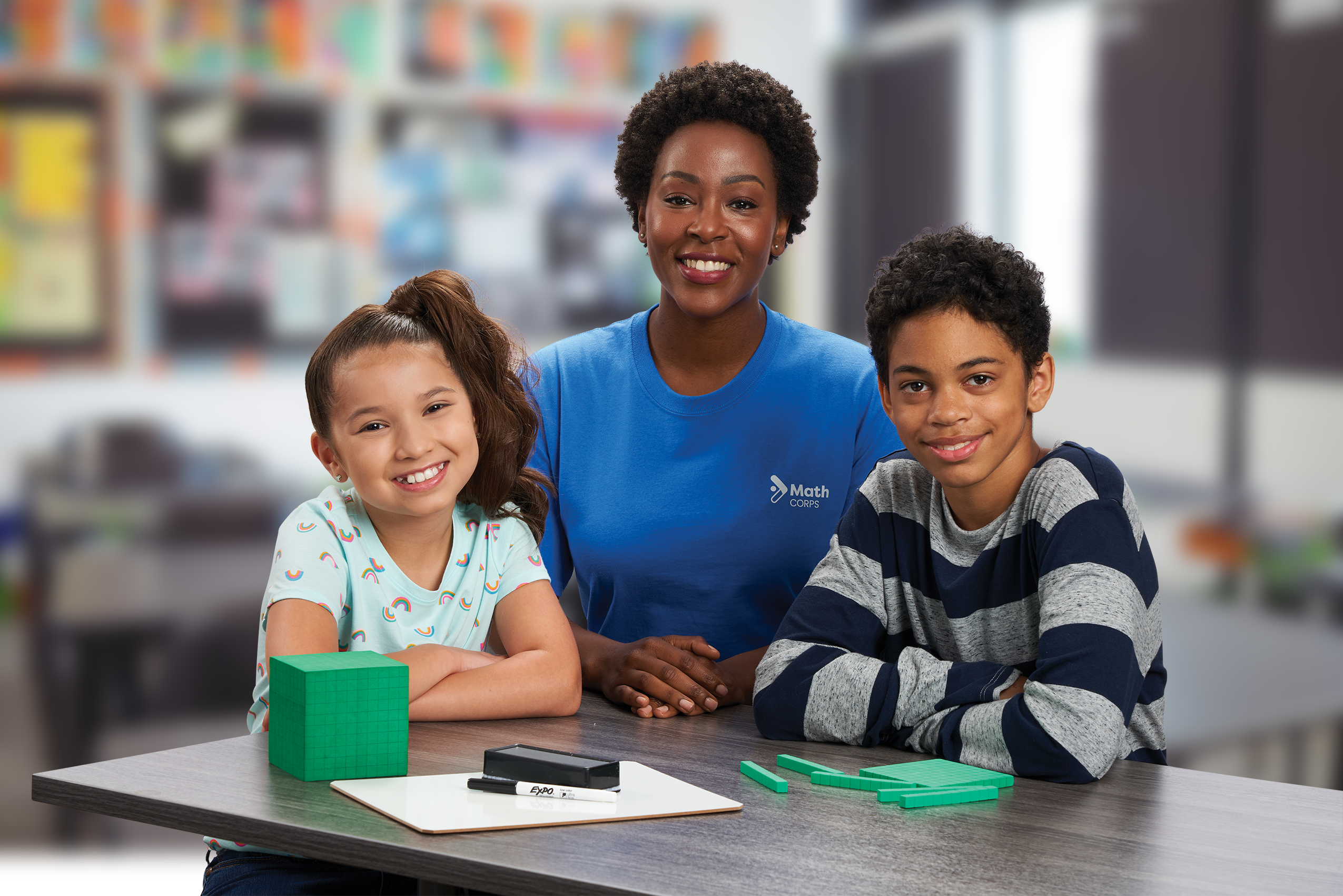 K-3 Math tutor and two students smiling at a desk with a math intervention.