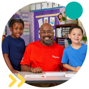 Reading Corps tutor smiling during a reading intervention with two male students.
