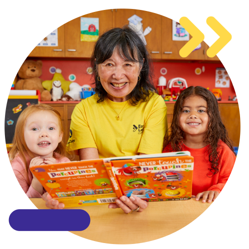 Early Learning tutor  reading a book, smiling with two preschool students in Early Learning Corps.